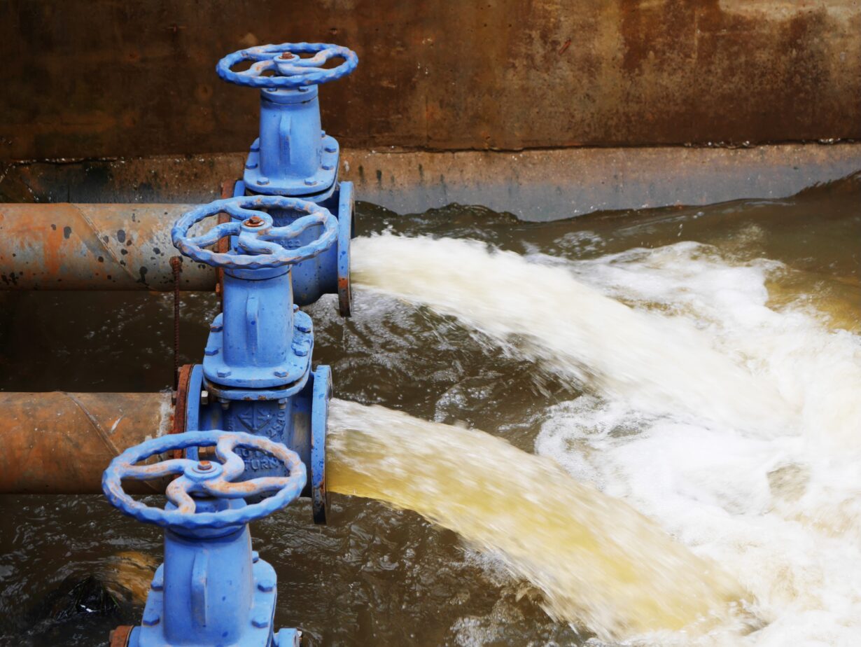 Industrial drainage system with five blue pipes discharging water into a reservoir. Concept of water management, wastewater treatment, and environmental engineering, spillway