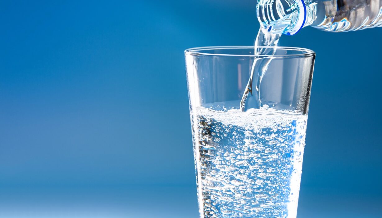 pouring water into a water glass, isolated drinking glass in front of a bright blue sunny and abstract background, close-up of a carbonated refreshing mineral water, beautiful concept with copy space